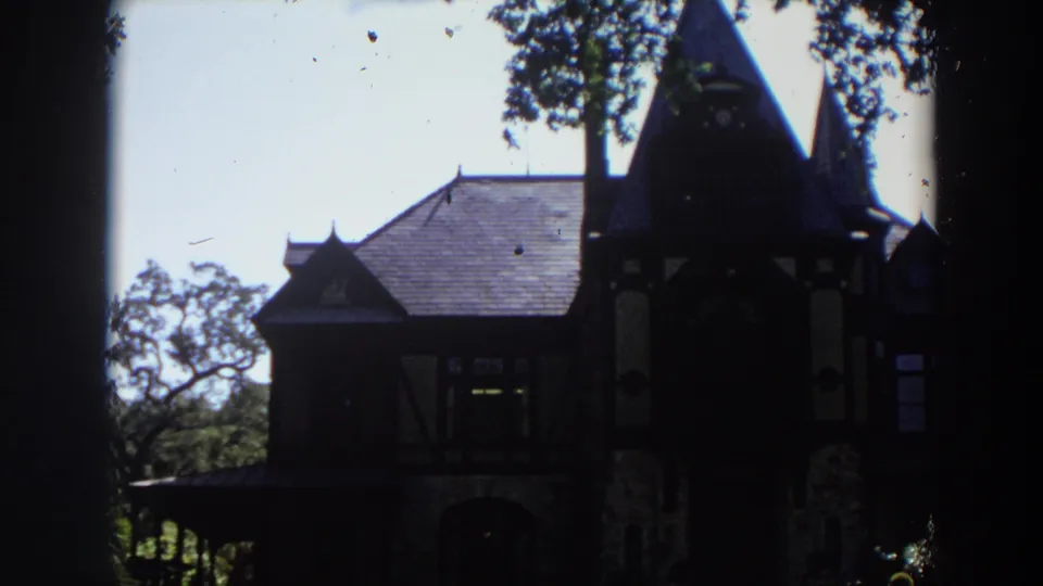 1964 California 8mm frame where the old stone-and-timber house falls into heavier shadow beneath trees.
