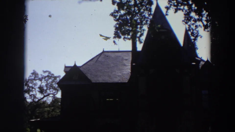 1964 California 8mm frame showing a silhouetted old chapel-like exterior with spires, trees, and bright sky.