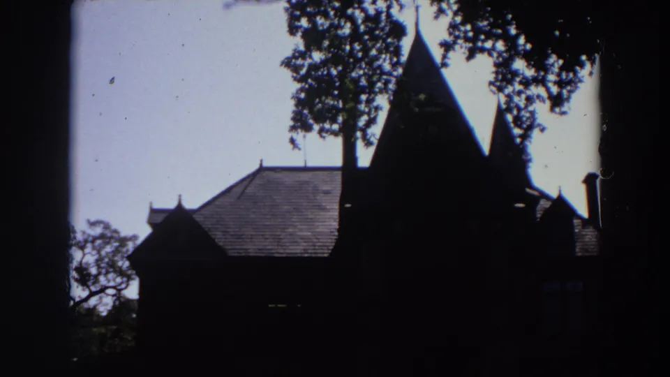 1964 California 8mm still with a shadowed chapel-like exterior, pitched roof, pointed spire, trees, and film dust.