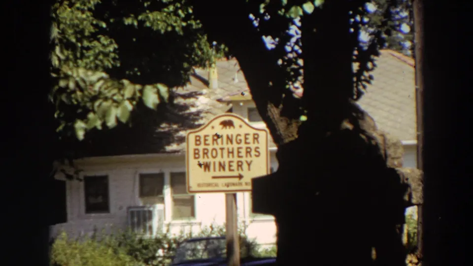 1964 California 8mm frame showing the Beringer Brothers Winery sign with dark tree framing and a pale building in the background.