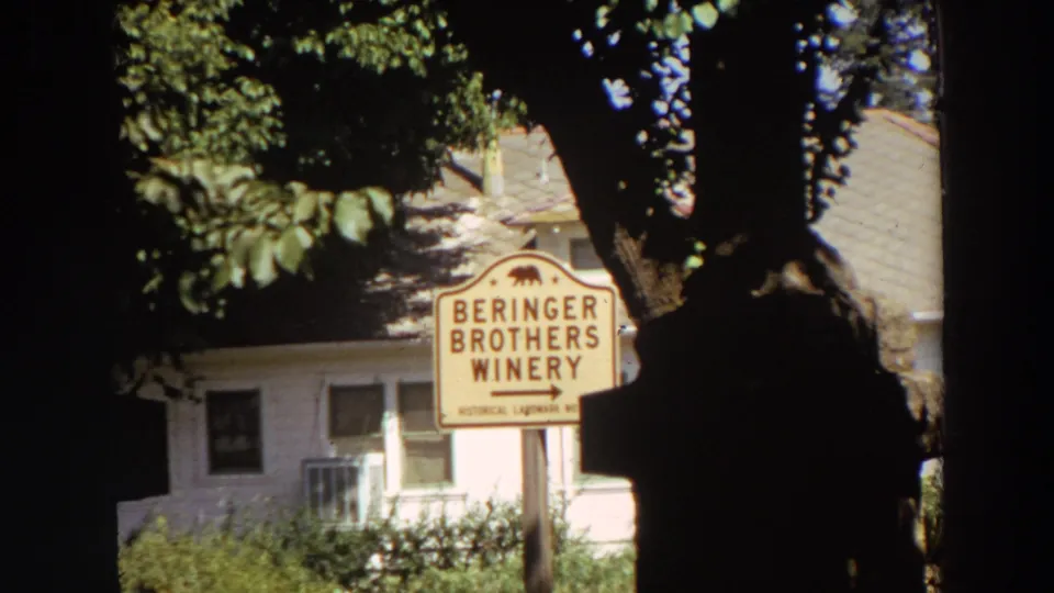 1964 California 8mm frame showing a Beringer Brothers Winery sign in tree shade near a pale roadside building.