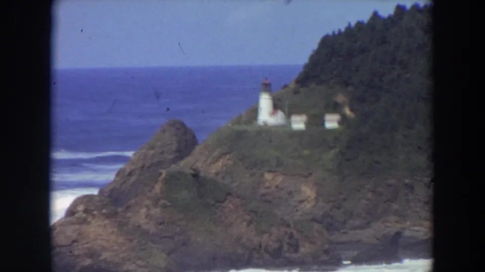 Soft 8mm frame of a California lighthouse on a green coastal bluff above waves and rocks.