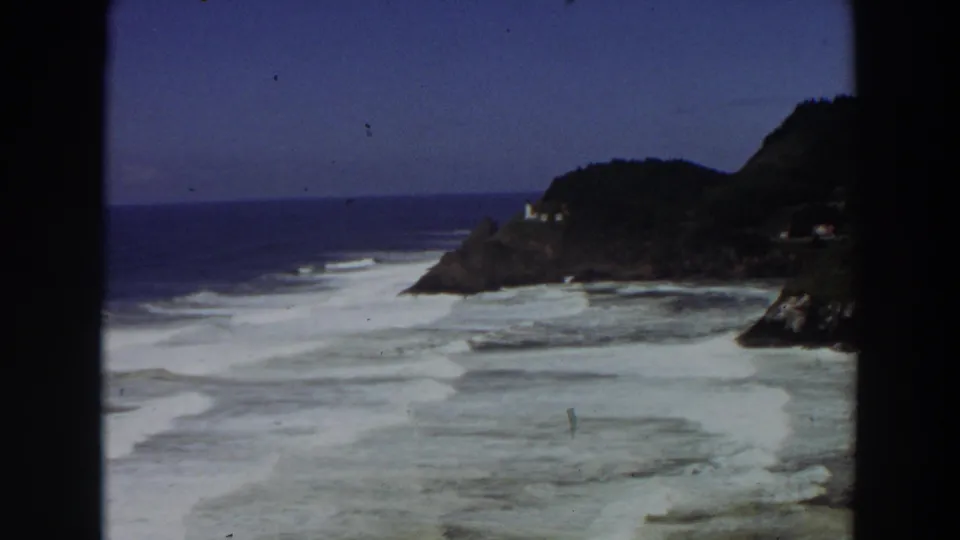 Late-frame 1964 California coastline view with a small lighthouse on the headland and white surf filling the foreground.
