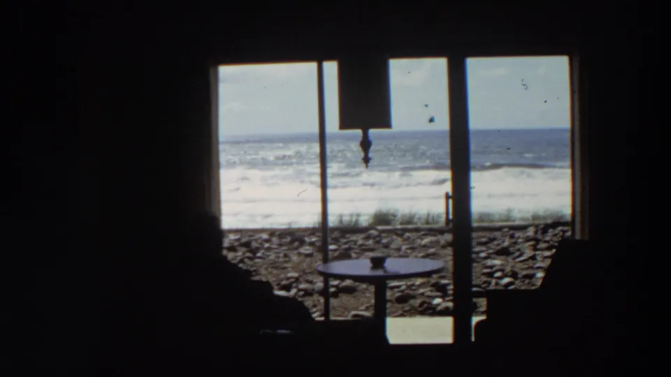 1964 California 8mm frame with the seated figure still in silhouette while bright Pacific surf fills the window view.