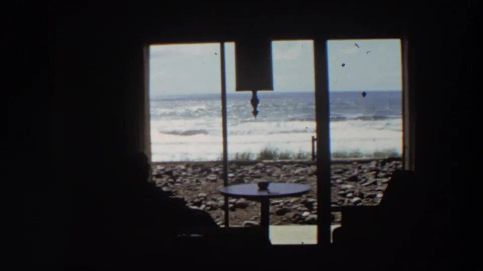 Final 1964 California coastal frame holds on the silhouetted viewer, window grid, small table, and waves beyond the shore.
