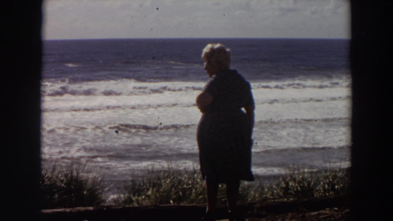 Elderly woman in silhouette stands by a grassy ocean overlook.