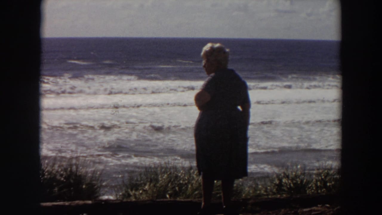In this 1964 California 8mm frame, the woman appears in profile against bright Pacific surf and a distant horizon.