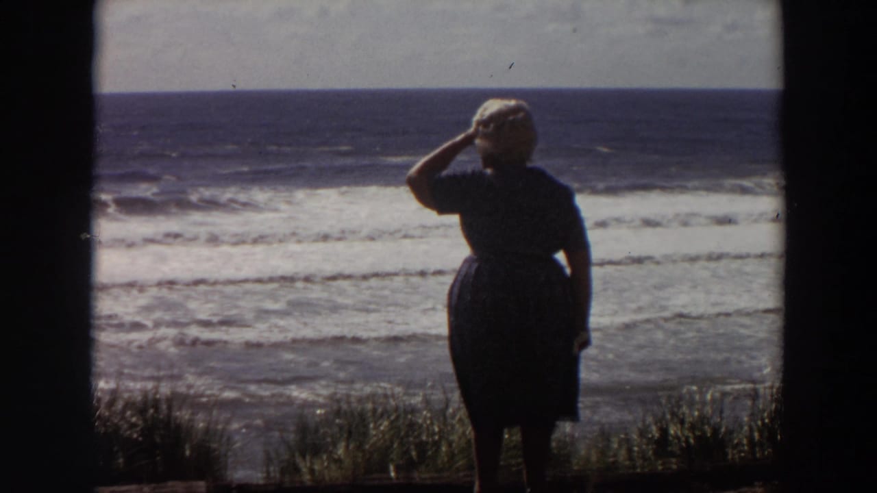 Woman raises a hand to her forehead while facing the ocean surf.