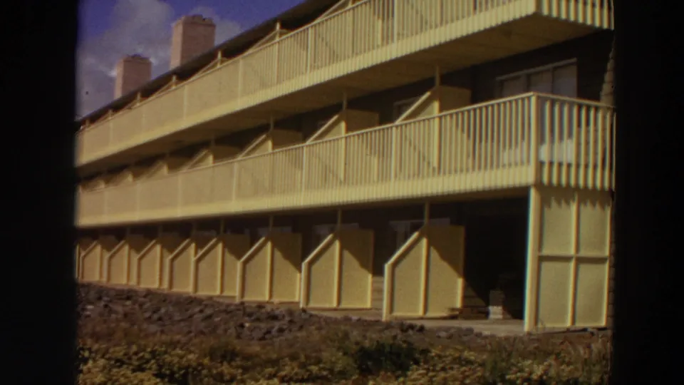 Yellow mid-century motel exterior in California, showing stacked exterior balconies, railings, doors, and a low planted foreground.
