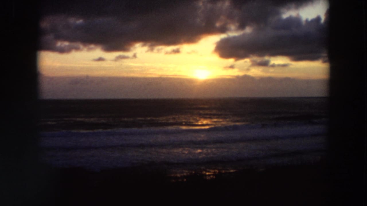 Golden sun near the ocean horizon with clouds above and surf below, framed by dark edges.