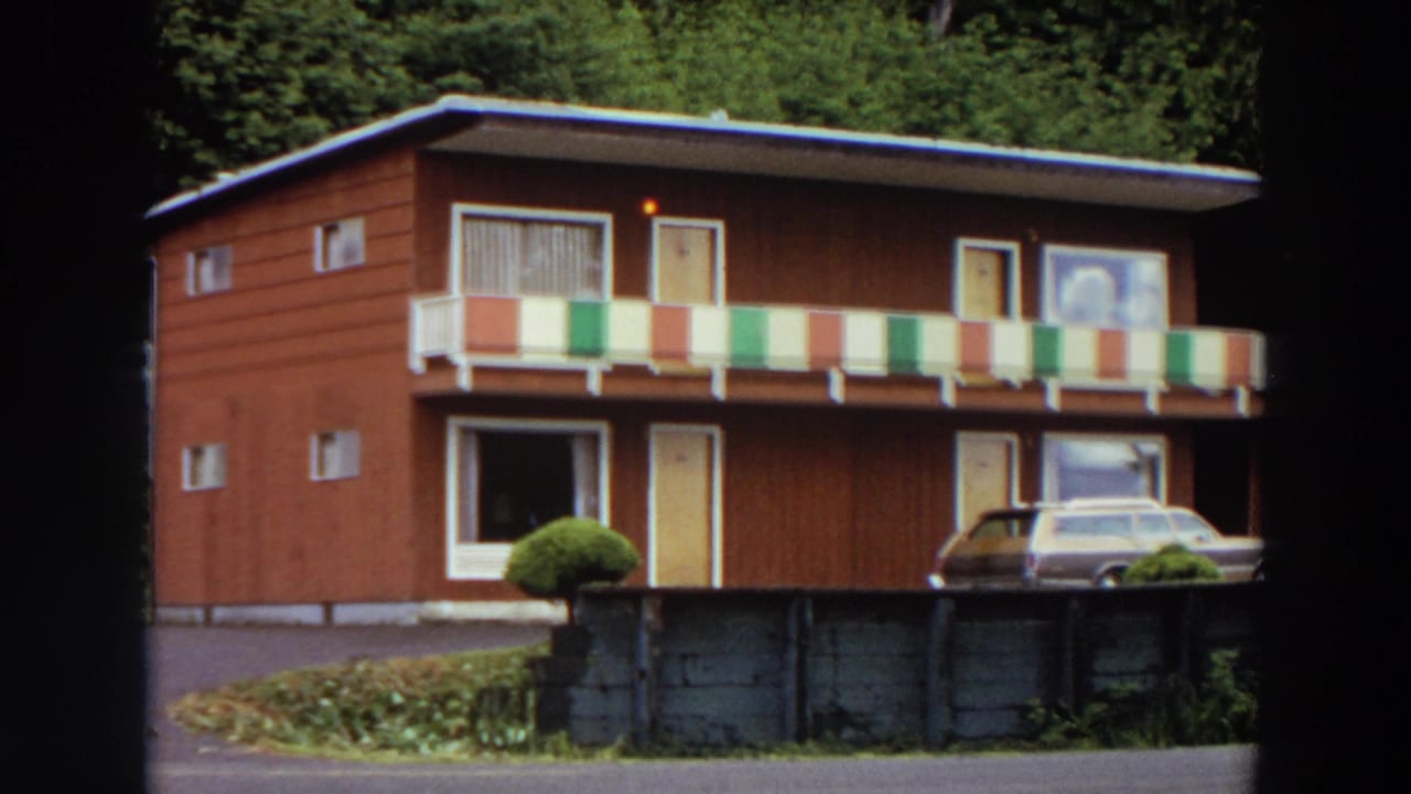 Two-story red motel with striped balcony railing and a station wagon parked in front.