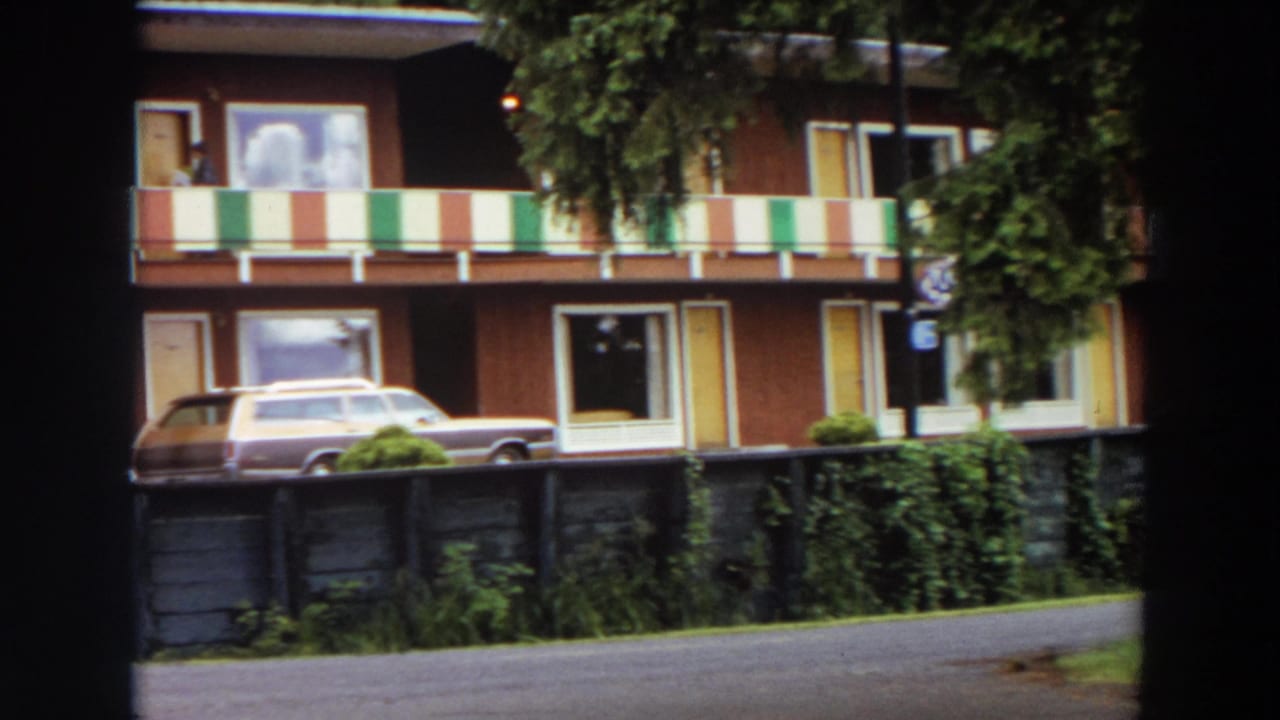 Apartment facade with striped balcony panels and a station wagon parked in front.