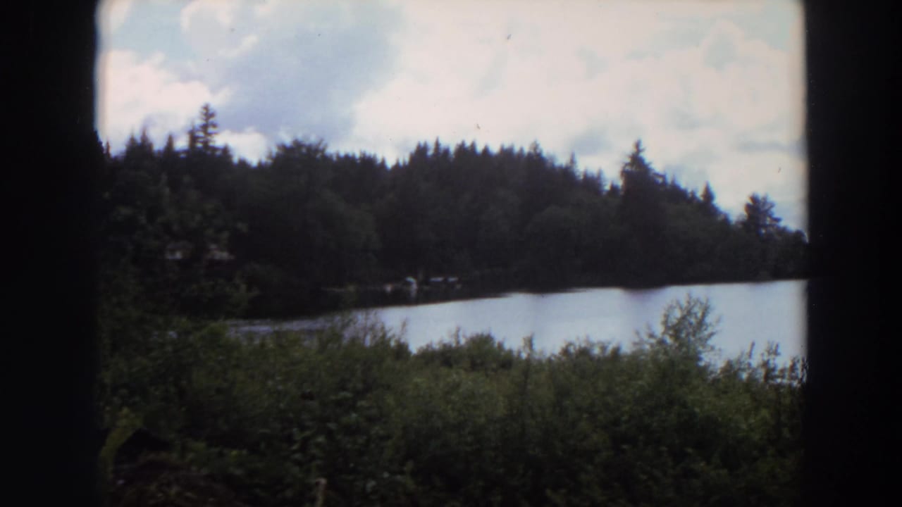 Lake and evergreen shoreline under a cloudy sky, framed by dark edges.