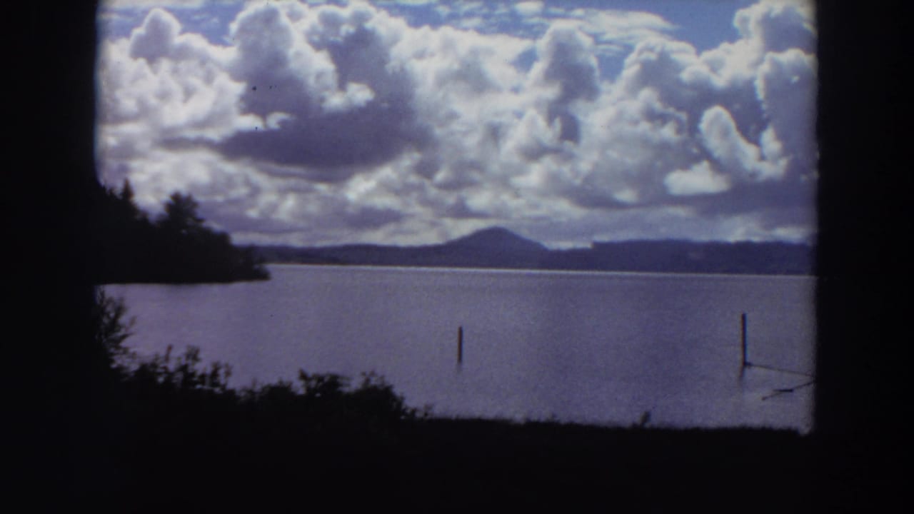 Lake and mountain horizon beneath bright clouds, with posts in the water.