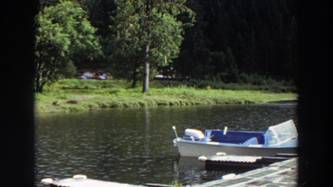 Empty white motorboat with blue interior beside a dock on a calm lake.