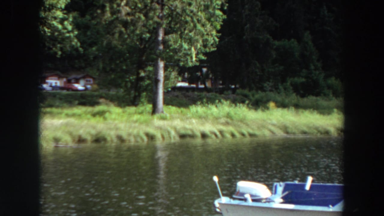Motorboat partly visible at the right edge beside lake water and a grassy, tree-lined shore.