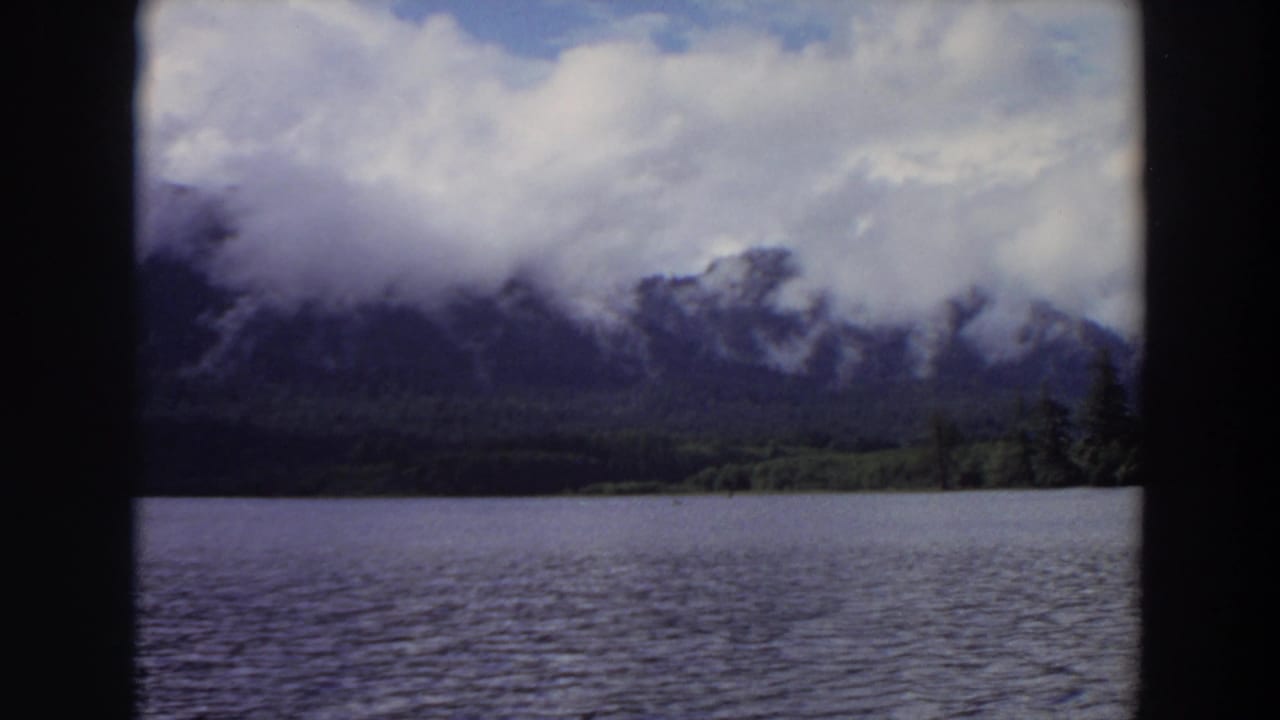 Rippling lake below cloud-covered mountains and a bright sky.
