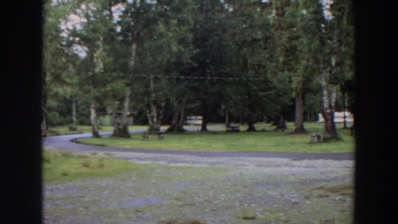 1964 California 8mm frame showing a quiet wooded park, curving gravel path, grass, benches, and dark foreground framing.
