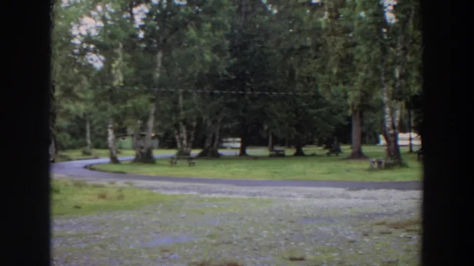 1964 California 8mm frame showing a quiet wooded park, curving gravel path, grass, benches, and dark foreground framing.