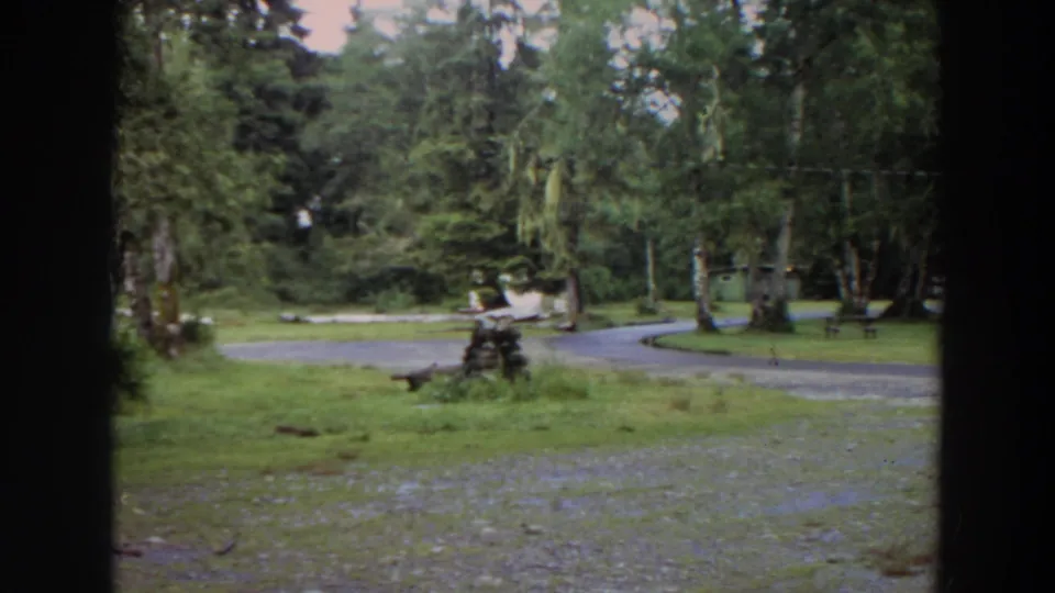 Late clip frame from 1964 California footage showing a wooded park, winding path, benches, grass, and dark foreground framing.