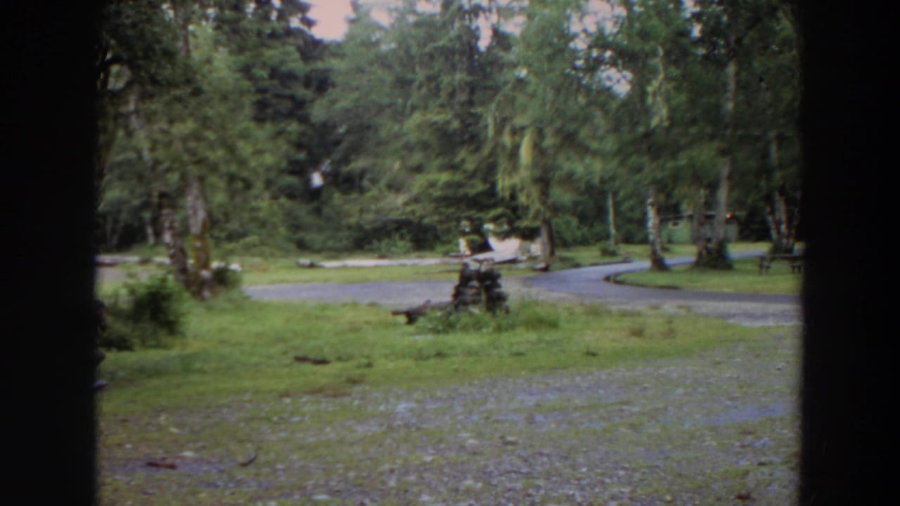Gravel path curves through a green wooded campground area with dark film-frame edges.