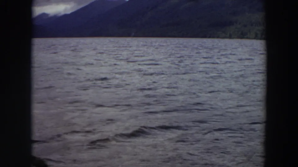 1964 Washington lake scene with wind-textured water, dark mountain forms, a distant tree line, and visible film-frame borders.