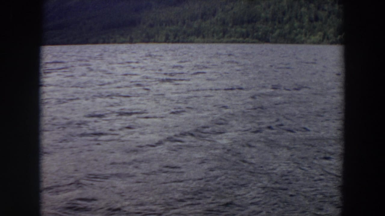 1964 Washington 8mm frame showing wind-ruffled lake water, wooded hills, and dark framing that suggests a boat window or film edge.