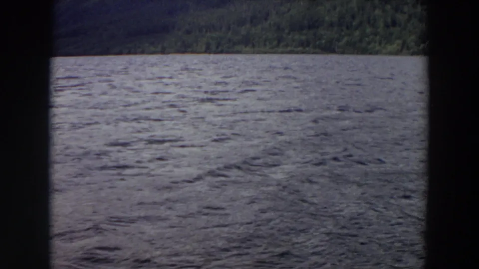 1964 Washington 8mm frame showing wind-ruffled lake water, wooded hills, and dark framing that suggests a boat window or film edge.