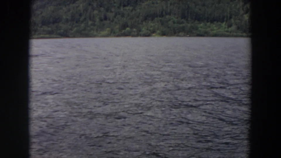 1964 Washington 8mm frame of rippling lake water and a distant forested shore seen through dark film or window borders.