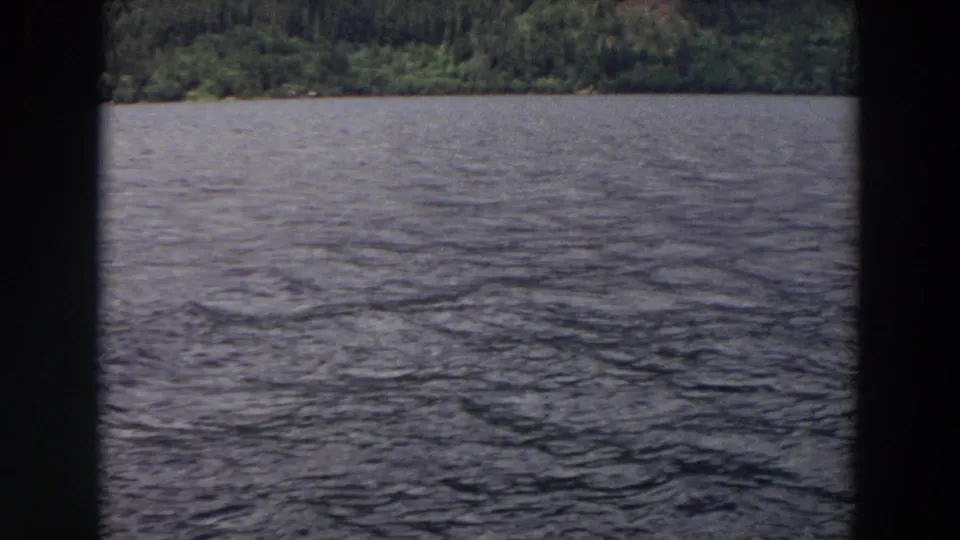 1964 Washington 8mm frame showing rippled lake water, a low wooded shoreline, and heavy dark borders at the sides.