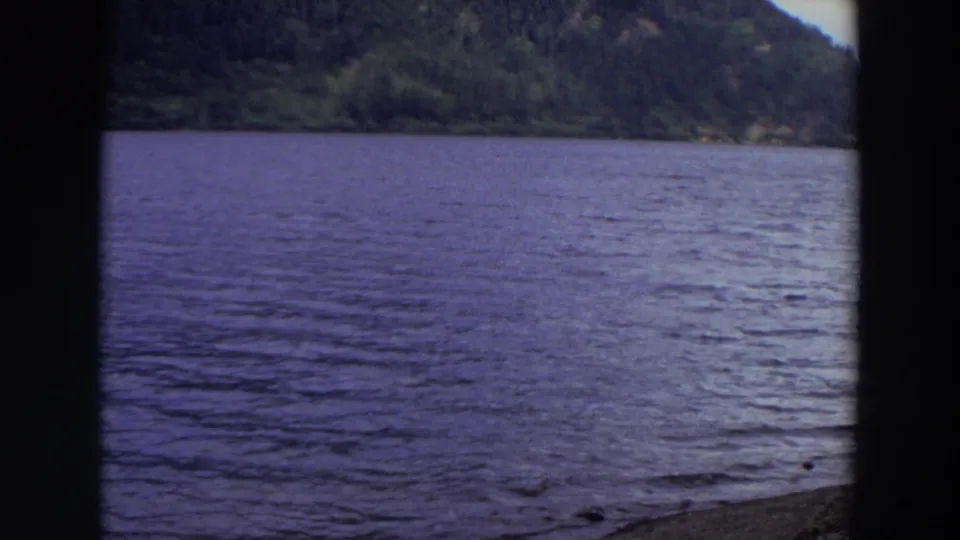 The closing frame looks across a calm Washington lake toward wooded hills, with visible 8mm frame edges.