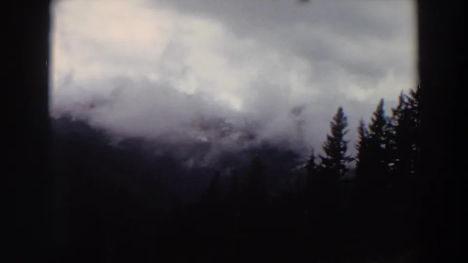 Misty Washington mountain scenery on 8mm film, with evergreen trees silhouetted against clouds and shadowed slopes.