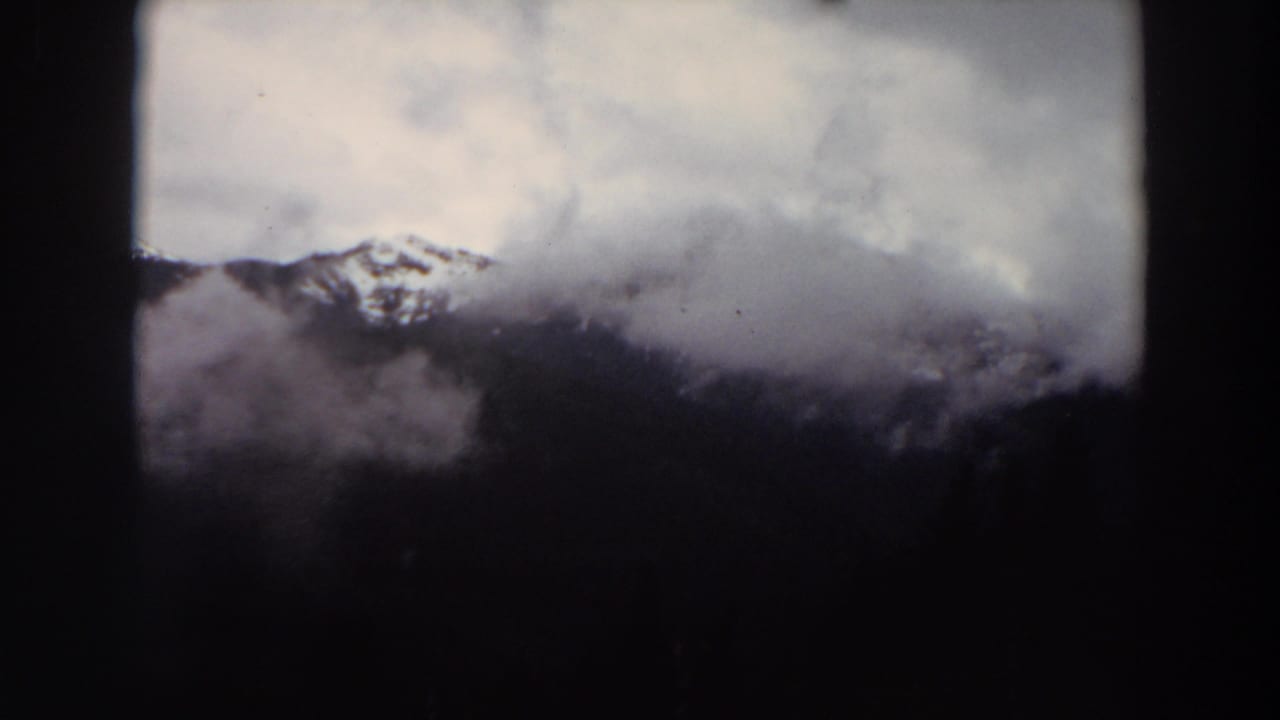 1964 Washington 8mm frame showing snow-capped mountains partly obscured by mist and a cloudy sky.