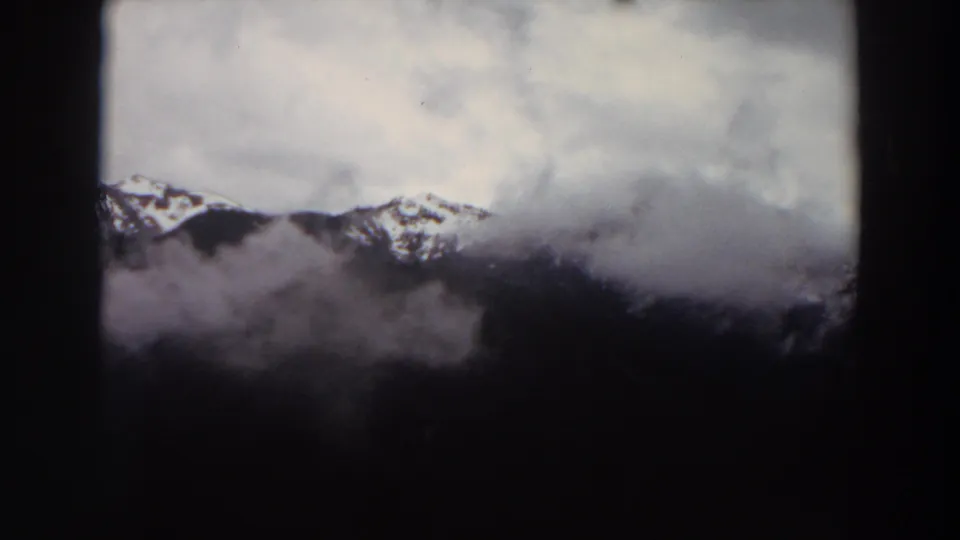 1964 Washington 8mm frame of a distant snowy ridge line under a gray, cloud-filled sky.
