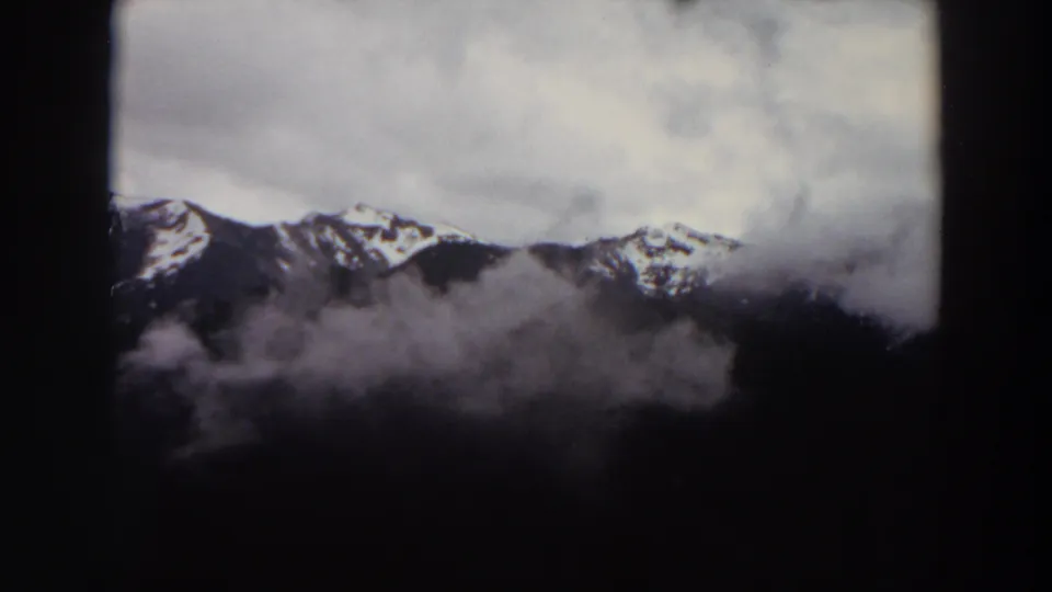 1964 Washington 8mm frame showing snow-patched mountains beneath layered cloud and mist.