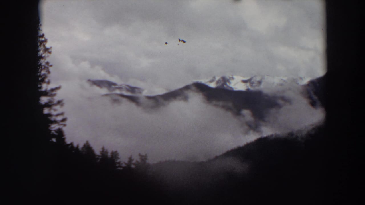Misty mountain peaks partly hidden by clouds above dark tree silhouettes.
