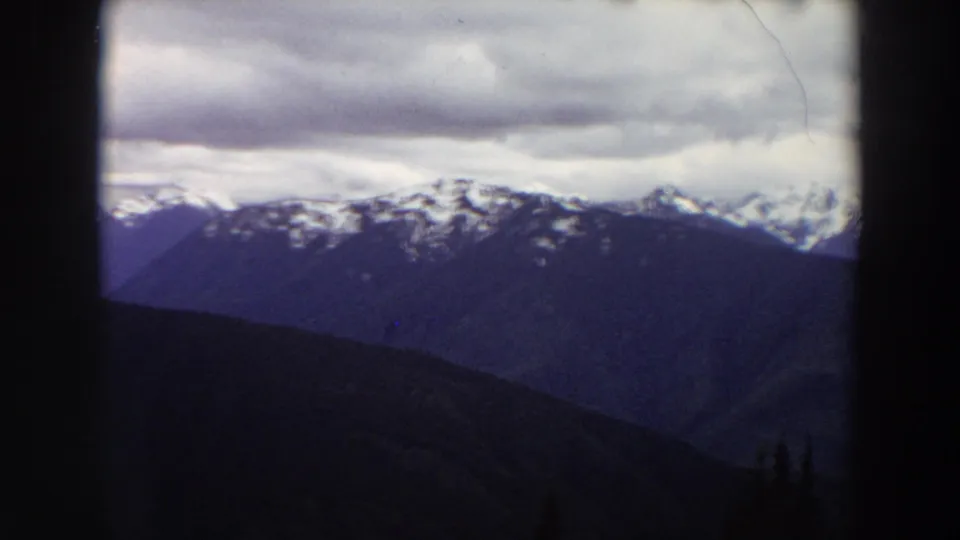Distant Washington mountain ridges appear in muted blue tones, with snow along the upper peaks and low cloud cover above.