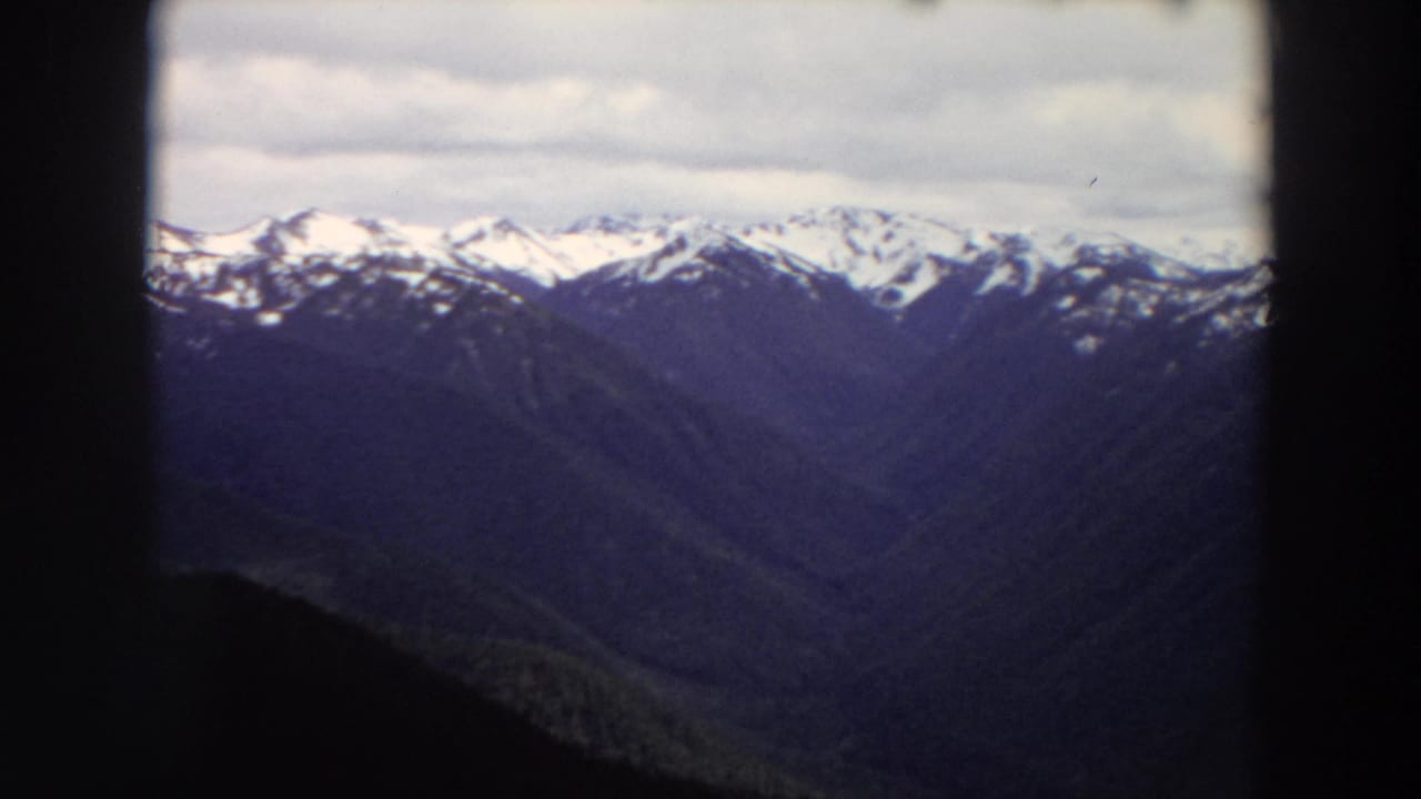 Snow-capped mountain range seen through a dark window-like frame.
