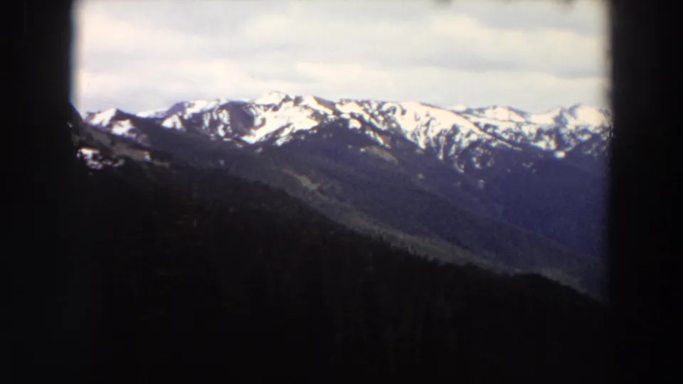 1964 Washington home-movie view of snow-capped peaks and blue ridges framed by a dark foreground edge.