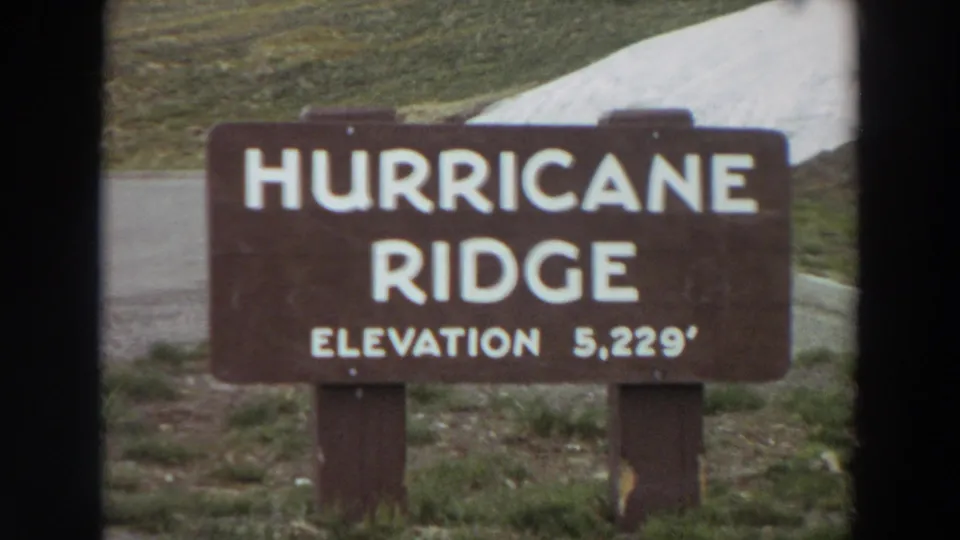 Final frame of the 1964 Washington clip showing the Hurricane Ridge elevation sign against grass, pavement, and a snow slope.