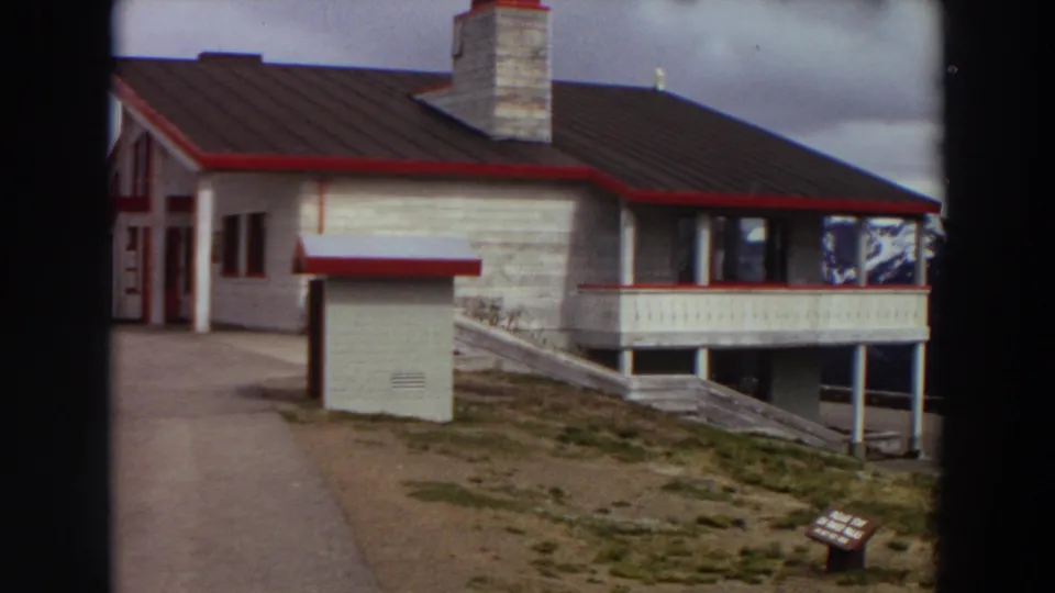 1964 Washington 8mm frame showing the building facade, red trim, porch railing, chimney, and cloudy mountain-area setting.