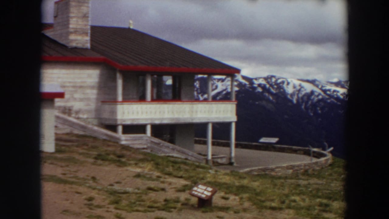 Lodge balcony and roofline beside a snowy mountain range.