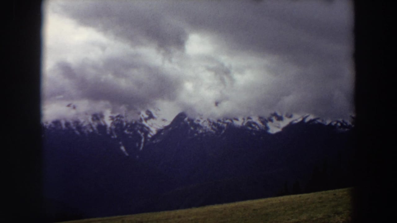 Snow-capped mountain range under heavy clouds with dark film borders.