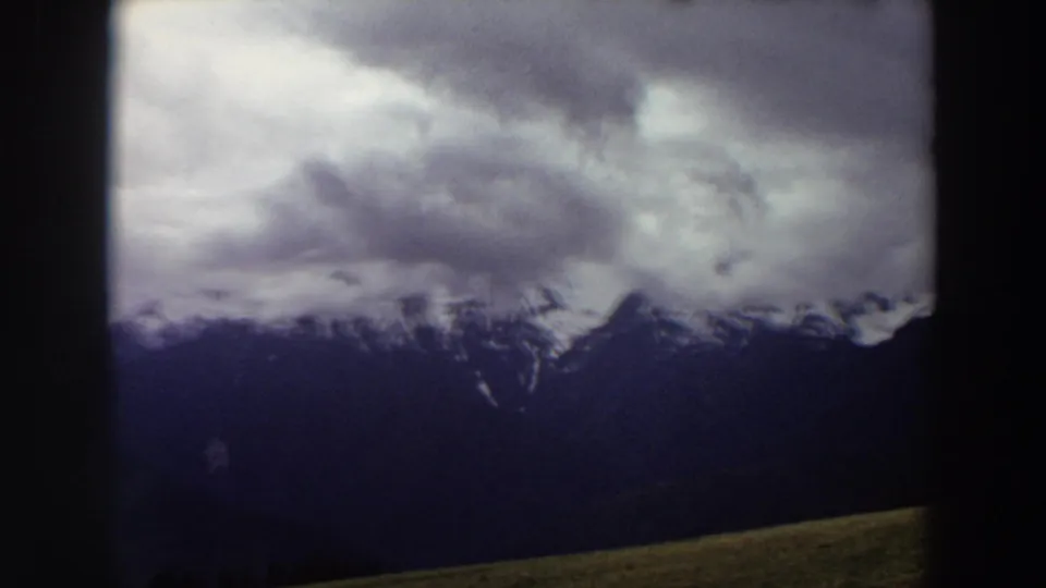 1964 Washington mountain vista with snow-bright peaks, dense cloud cover, and a dark foreground slope in 8mm color.