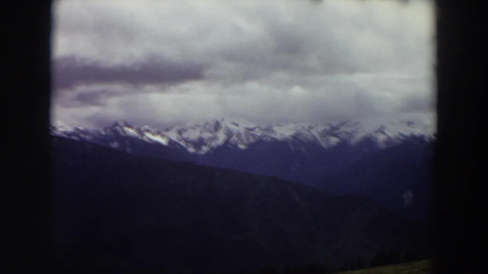 Cloudy 1964 Washington mountain view on 8mm film, with snow-bright peaks behind darker hills.