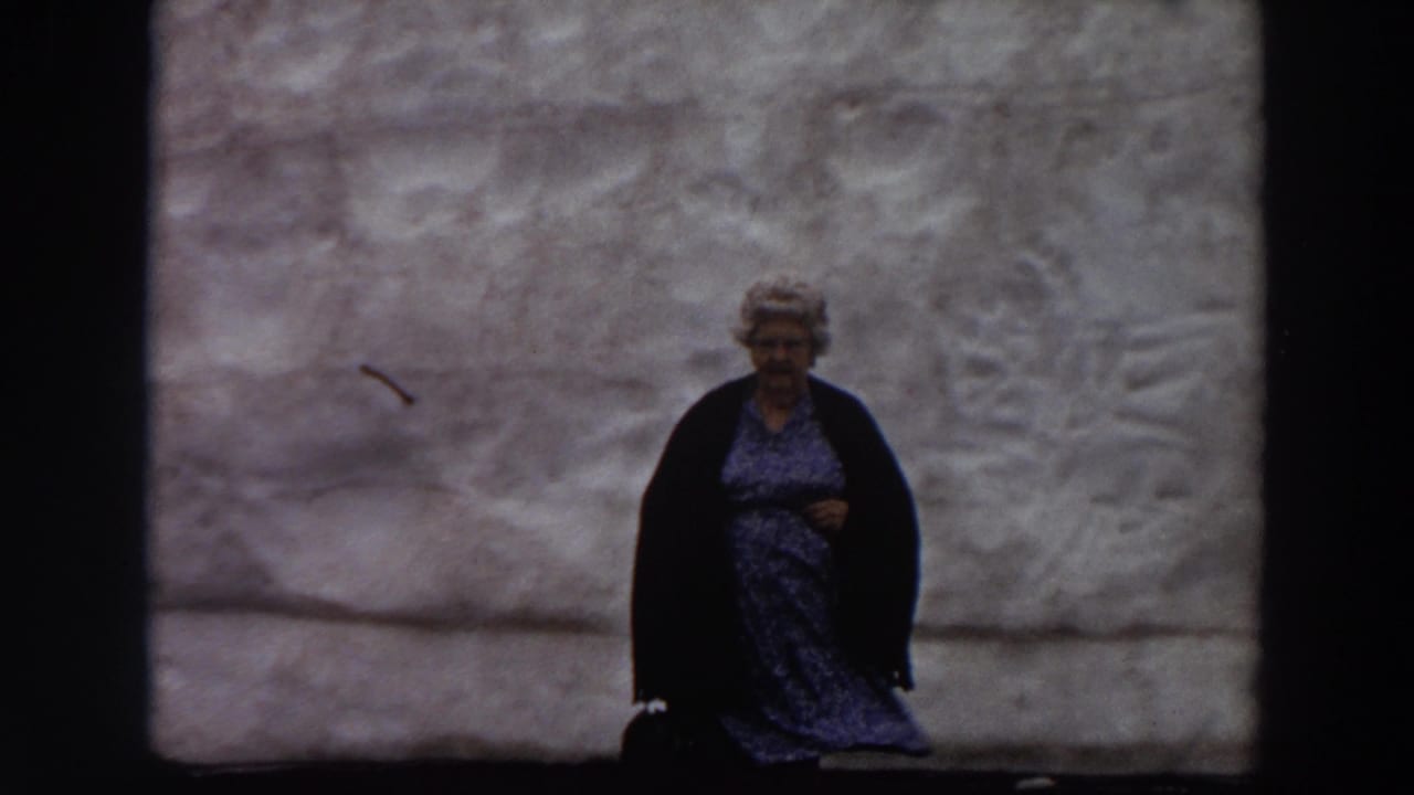 Woman in a blue dress and dark cardigan stands before a large textured grey wall.