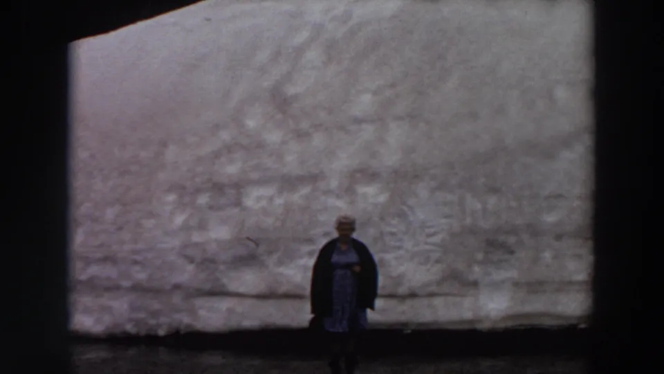 The 8mm frame shows the woman low in the composition, standing still before a wide pale grey textured wall in Washington.