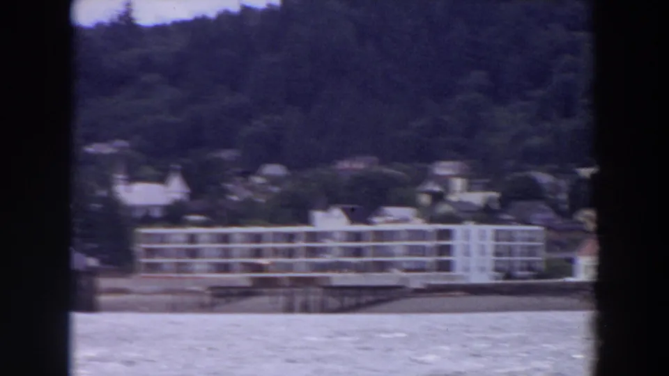 A large white multi-story waterfront building stands near smaller houses along a Washington lakeshore in 1964 footage.