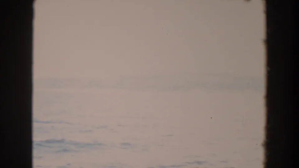 Bright, washed 8mm frame from the Washington boat sequence, showing pale water, faint horizon, and dark film border.