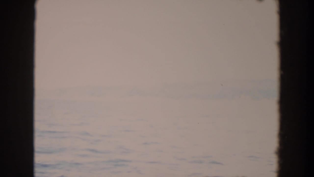 1964 Washington 8mm view of a pale misty ocean horizon with faint distant land and dark vertical edges in the frame.